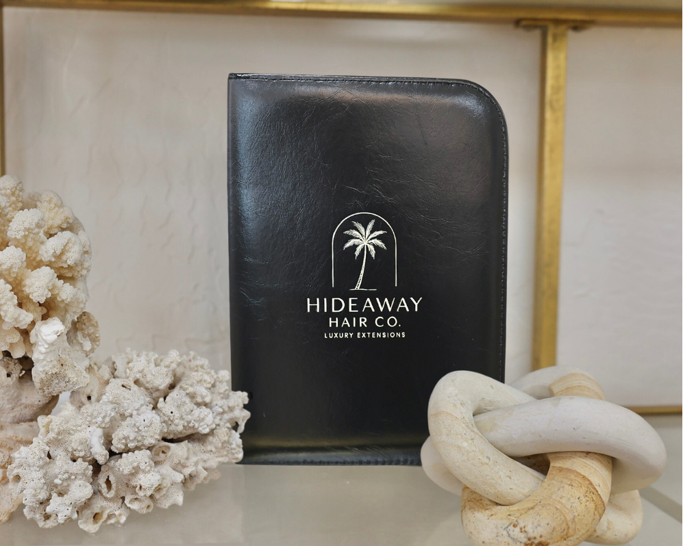 Black leather case with 'Hideaway Hair Co' logo on a decorative surface with coral and stone sculpture.